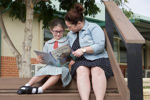 teacher and student sitting on steps reading a book